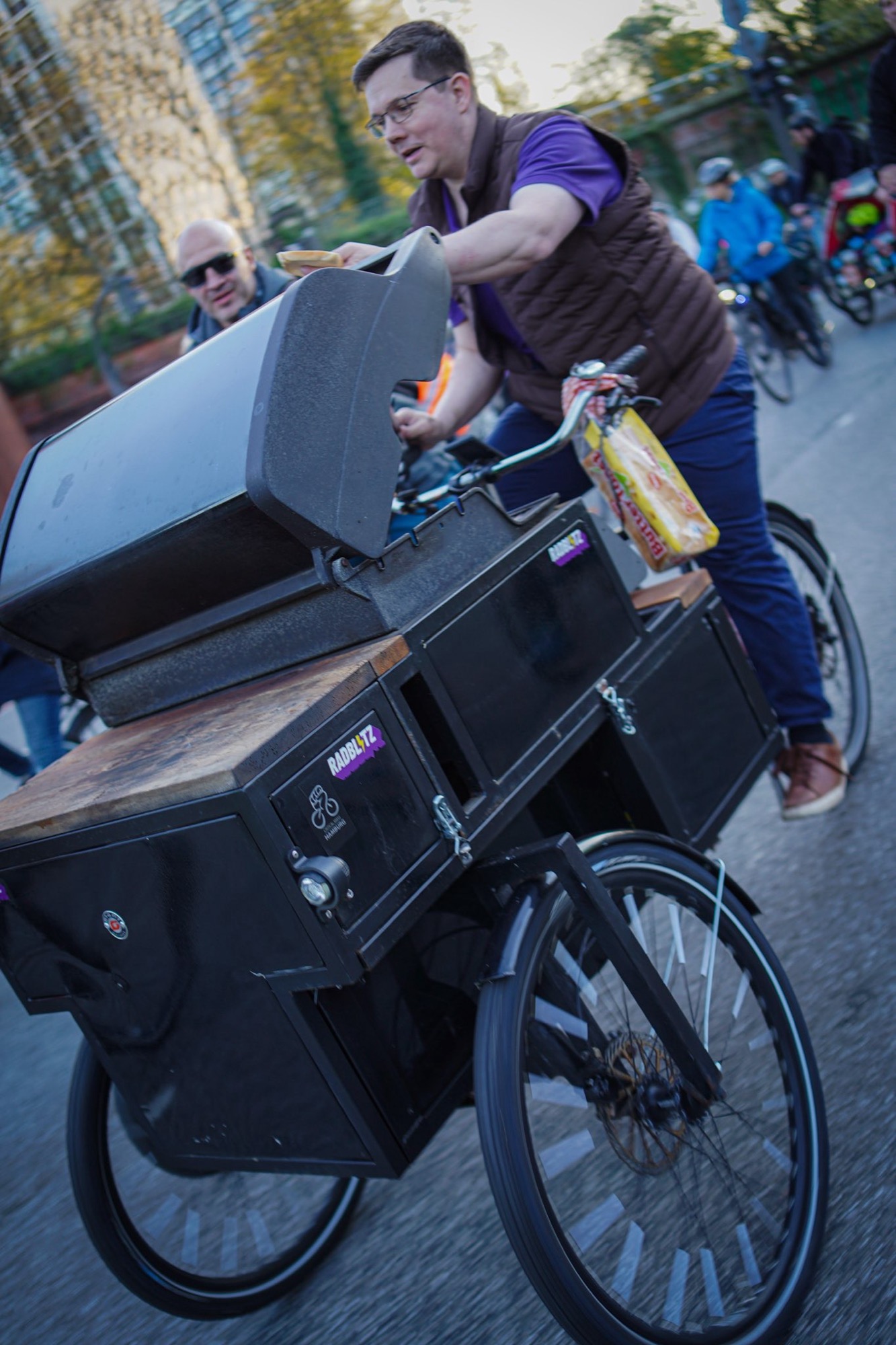 Jonas reicht während der Critical-Mass-Fahrt einen Hotdog vom Grillfahrrad